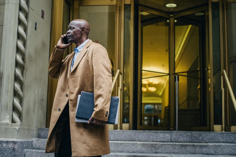 a man in a tan coat talking on a cell phone, a photo, by Andrew Stevovich, pexels contest winner, lawyer suit, tall entry, atiba jefferson, he is carrying a black briefcase