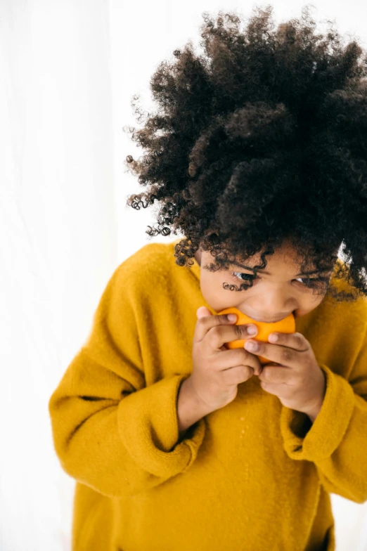 a little girl holding a pair of scissors in her hands, pexels, antipodeans, she is eating a peach, with afro, long orange sweatshirt, profile image