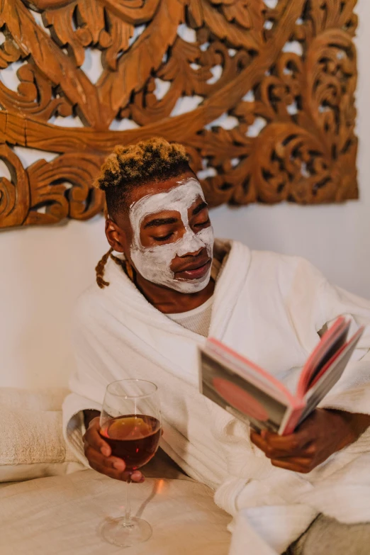 a man sitting on a bed reading a book, a portrait, by Cosmo Alexander, trending on pexels, afrofuturism, white facepaint, spa, themed after wine, face mask