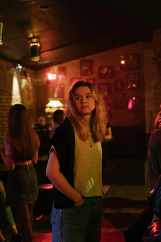 a group of people standing next to each other in a room, a portrait, by Alice Mason, pexels, happening, dimly lit dive bar, portrait of anya taylor-joy, walking to the right, a girl with blonde hair