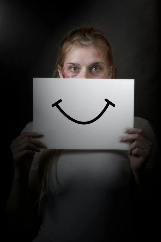 a woman holding a sign with a smiley face drawn on it, inspired by Odd Nerdrum, trending on pexels, horror smile, low key, dissection of happy, mugshot