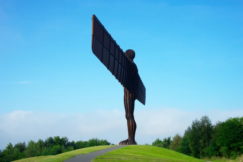 a large metal angel statue sitting on top of a lush green field, by John Henderson, pexels contest winner, new sculpture, north, narrow wings behind, tourist destination, architecture carved for a titan