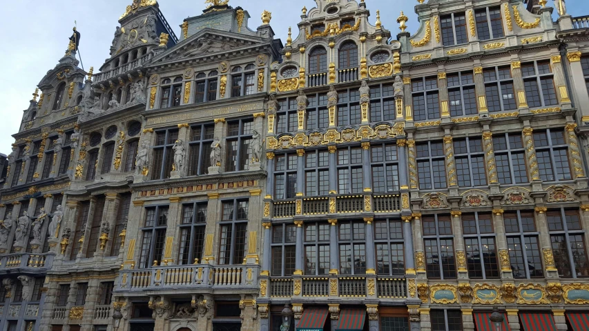 a group of people standing in front of a tall building, by Maria van Oosterwijk, pixabay, baroque, gold and cobalt tiles, mossy buildings, flanders, blue shutters on windows