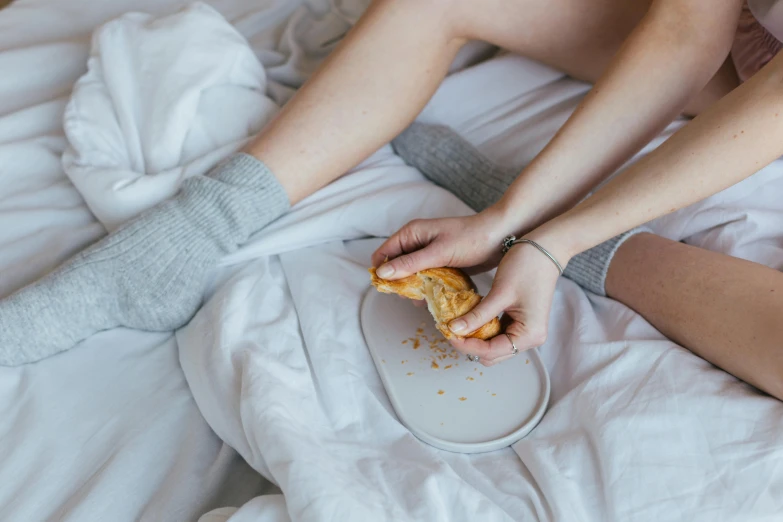 a person sitting on a bed eating a sandwich, inspired by Sarah Lucas, trending on pexels, holding hands, messy bed, eating garlic bread, grey