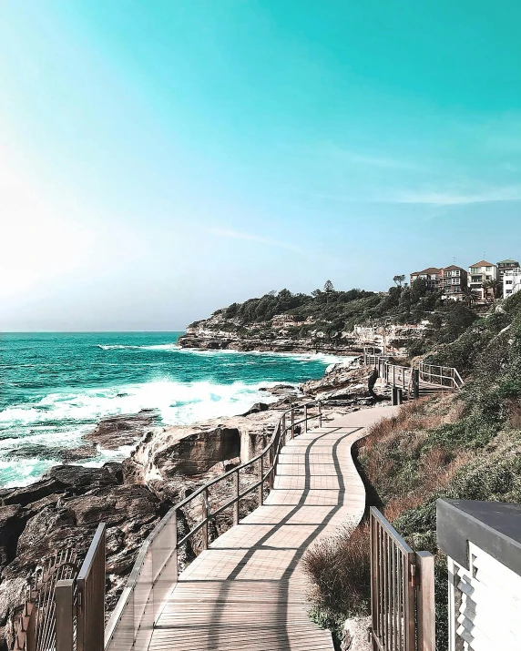 a wooden walkway leading to a beach next to the ocean, bondi beach in the background, teal aesthetic, staggered terraces, snapchat photo