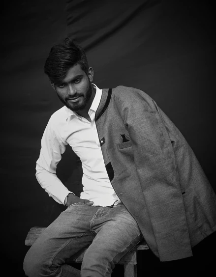 a black and white photo of a man sitting on a stool, a black and white photo, unsplash, hurufiyya, indian super model, dressed in a gray, portait photo profile picture, wearing jacket