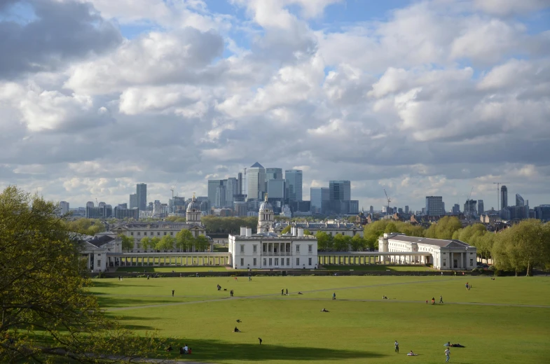 a group of people sitting on top of a lush green field, inspired by Rachel Whiteread, pexels contest winner, mannerism, skyline showing from the windows, park on a bright sunny day, square, olympics