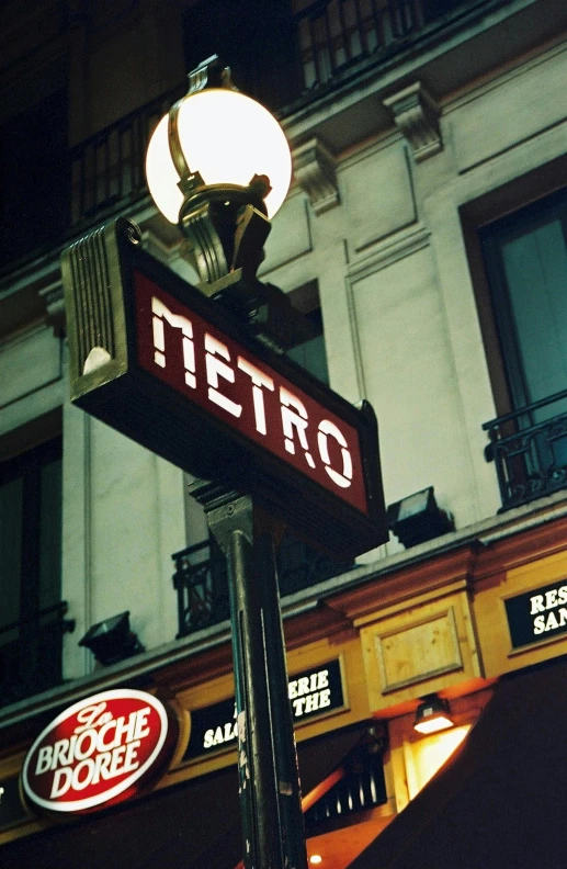 a close up of a street sign with a building in the background, inspired by Brassaï, metro, photo taken on fujifilm superia, station, beautiful lit