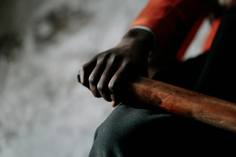 a close up of a person holding a baseball bat, inspired by Gordon Parks, visual art, sitting with wrists together, dark grey and orange colours, dark skin, thumbnail