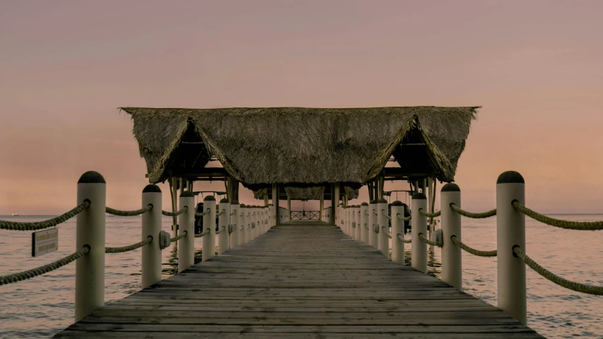 a dock in the middle of a body of water, thatched roof, in the evening