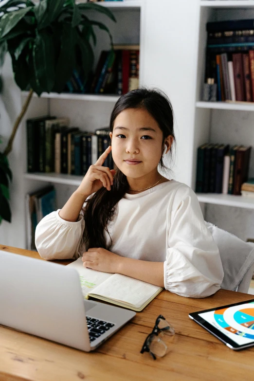 a woman sitting at a table in front of a laptop computer, young asian girl, with a pointed chin, educational supplies, wearing a cute top