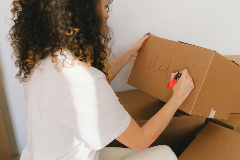 a woman sitting on the floor holding a cardboard box, a cartoon, by Julia Pishtar, pexels contest winner, whiteboards, brown curly hair, close-up shot from behind, maintenance photo