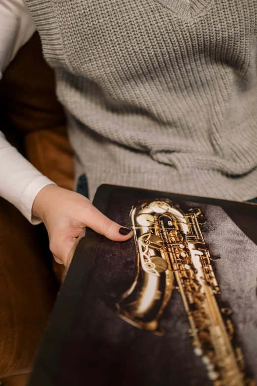 a woman sitting on a couch holding a book, an album cover, by Adam Marczyński, pexels contest winner, photorealism, real saxophones, high angle close up shot, metal plate photograph, old photobook