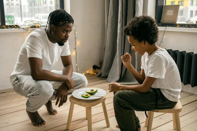 a man sitting on a stool next to a little boy, pexels contest winner, avacado chairs, dark-skinned, ready to eat, looking at each other mindlessly