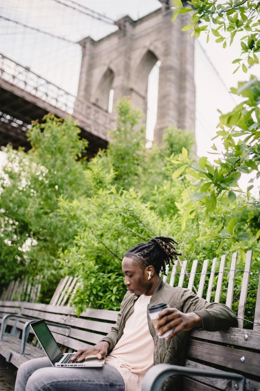 a man sitting on a bench using a laptop, by Nyuju Stumpy Brown, trending on unsplash, visual art, archways made of lush greenery, brooklyn, woman drinking coffee, standing on a bridge