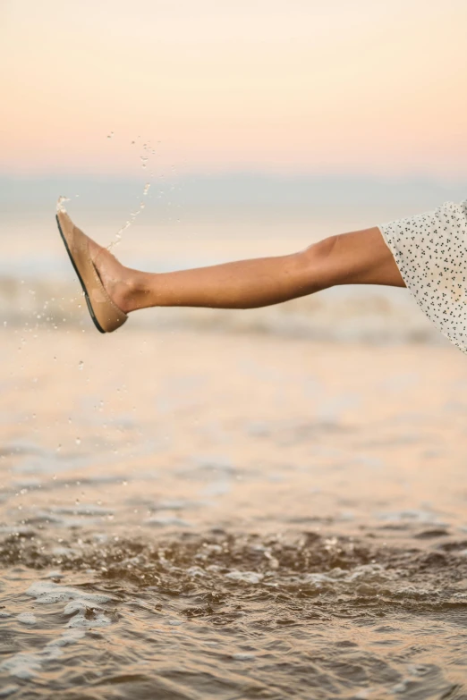 a woman standing in the water with her legs in the air, unsplash, arabesque, detailed foot shot, tan, flying through the air, ( ( ( ( kauai ) ) ) )