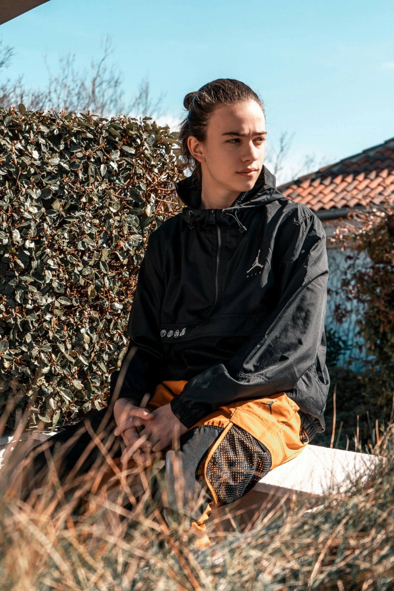 a woman sitting on a bench in front of a bush, a portrait, by Julia Pishtar, unsplash, black and yellow tracksuit, heron preston, profile image, black and orange