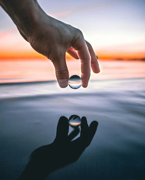 a person holding a ring over a body of water, glass ball, reaching out to each other, instagram picture, no watermarks