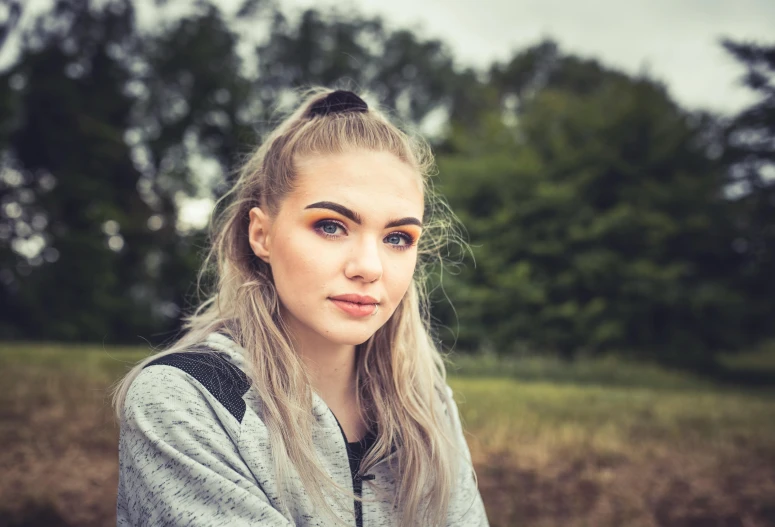 a woman sitting in a field with trees in the background, a picture, inspired by Elsa Bleda, shutterstock, realism, girl silver ponytail hair, 🤤 girl portrait, very high quality face, portrait of kim petras