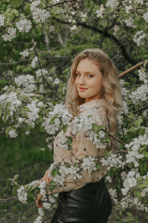 a woman standing in front of a flowering tree, an album cover, pexels contest winner, pale skin curly blond hair, russian girlfriend, background image, casual pose