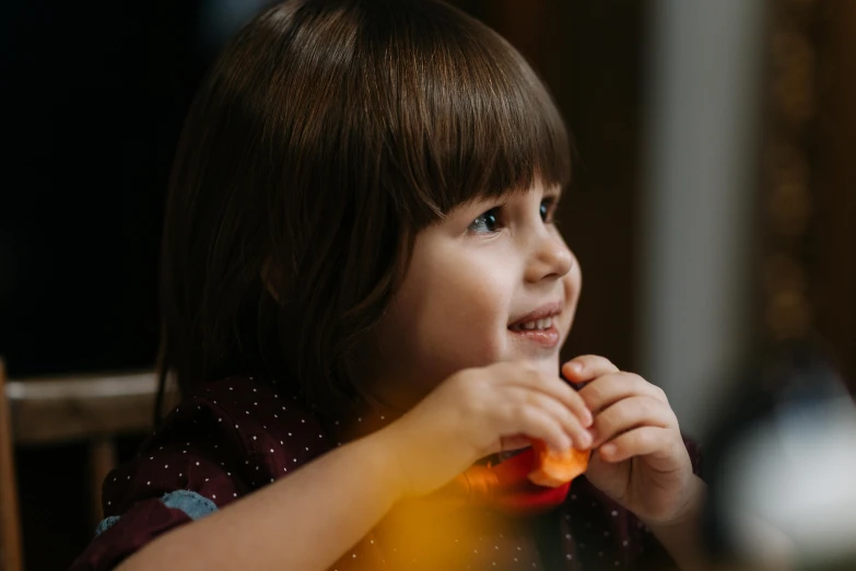 a little girl sitting at a table eating a carrot, by Adam Marczyński, pexels contest winner, bokeh top cinematic lighting, smiling girl, looking from side, girl with dark brown hair