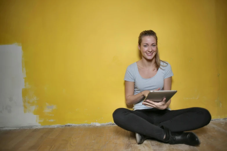 a woman sitting on the floor using a tablet computer, a portrait, inspired by Sarah Lucas, pexels contest winner, yellow wallpaper, wall painting, while smiling for a photograph, student