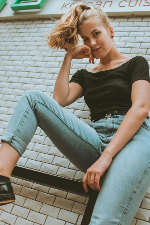 a woman sitting on a bench in front of a building, a colorized photo, trending on pexels, jeans pants, wearing a black t-shirt, high angle, portrait featured on unsplash