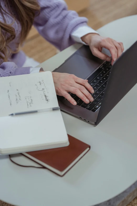 a woman sitting at a table using a laptop computer, multiple stories, high-quality photo, bottom angle, holding books