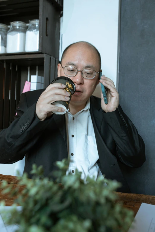 a man sitting at a table talking on a cell phone, inspired by Fei Danxu, pexels contest winner, wearing gold glasses, coffee smell, balding, wearing a black noble suit