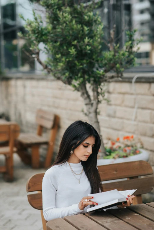 a woman sitting at a table reading a book, by Niko Henrichon, pexels contest winner, female with long black hair, sitting on a bench, a handsome, ameera al-taweel