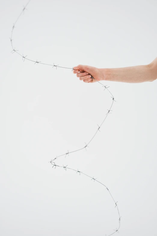 a person holding a string in their hand, an album cover, by Cerith Wyn Evans, unsplash, tracks of barbed wire, white background, environment, ignant