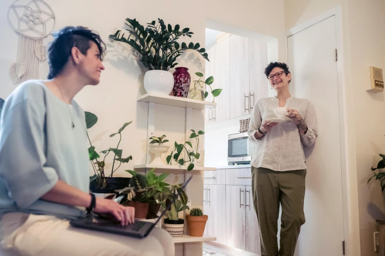 a couple of people that are standing in a room, home office, next to a plant, lachlan bailey, two women