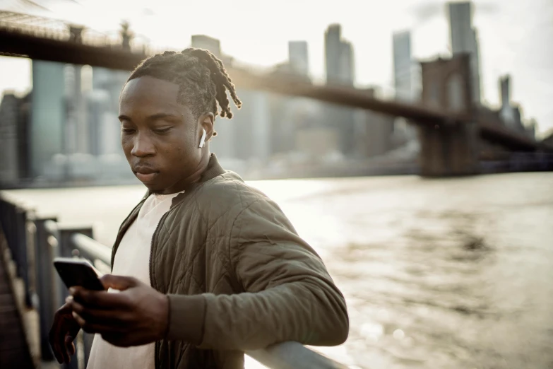 a man with dreadlocks looking at his cell phone, trending on pexels, city in background, on a bridge, earbuds, black teenage boy