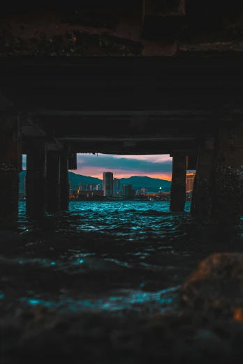 a view of a city from under a bridge, a picture, unsplash contest winner, the ocean in the background, colorful and dark, a still of kowloon, abandoned structures