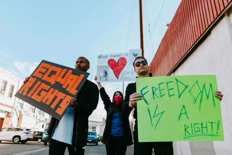 a group of people holding signs on a city street, by Julia Pishtar, pexels, rafeal albuquerque, the three moiras, brittney lee, square