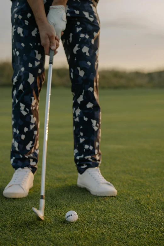 a man standing on top of a green field holding a golf ball, patterned clothing, wearing pants, thumbnail, video