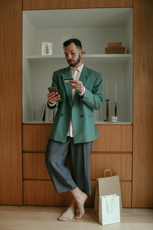 a man standing in a room holding a cell phone, by Sven Erixson, trending on pexels, hyperrealism, wearing green suit, at home, large pants, wearing business casual dress