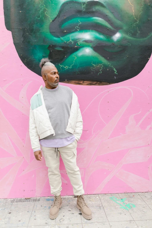 a man standing in front of a wall with a painting on it, an album cover, inspired by Terrell James, trending on unsplash, pink white and green, calm weather, casual pose, big floppa