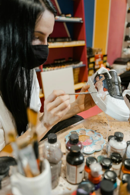 a woman sitting at a table working on a piece of art, an airbrush painting, trending on pexels, sneaker made out of lego, lacquerware, avatar image, stitching