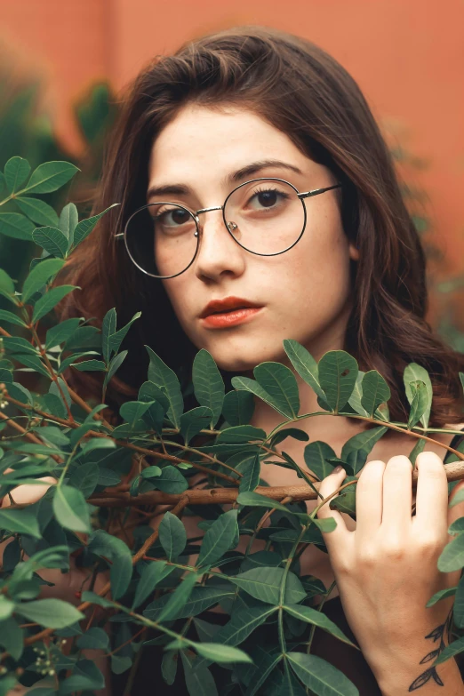 a woman wearing glasses standing next to a bush, a picture, inspired by Elsa Bleda, trending on pexels, square rimmed glasses, high-quality photo, woman made of plants, with deep green eyes