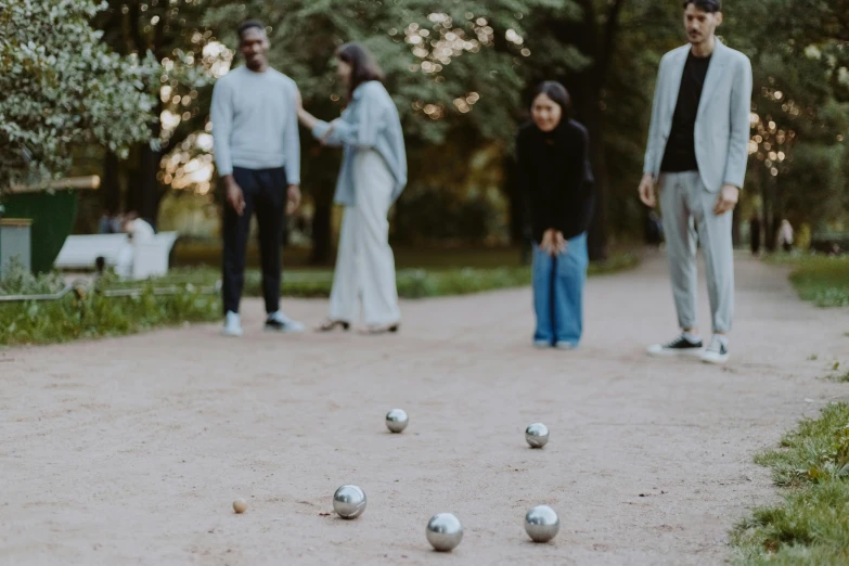 a group of people playing a game of boccup, by Emma Andijewska, pexels contest winner, interactive art, parks and gardens, grey, holiday season, holding a ball