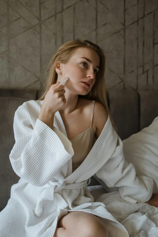 a woman sitting on a bed brushing her teeth, by Adam Marczyński, trending on pexels, happening, wearing nanotech honeycomb robe, holding a small vape, thick jawline, elegant lady with alabaster skin