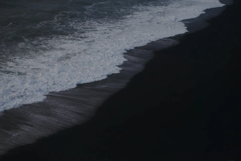 a man riding a surfboard on top of a wave covered beach, an album cover, inspired by Andreas Gursky, pexels contest winner, hurufiyya, black sand, moonless night, taken from a plane, clean detail 4k