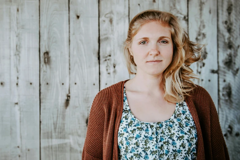 a woman standing in front of a wooden wall, a portrait, by Amalia Lindegren, unsplash, molly weasley, kim wexler, plain background, promo image