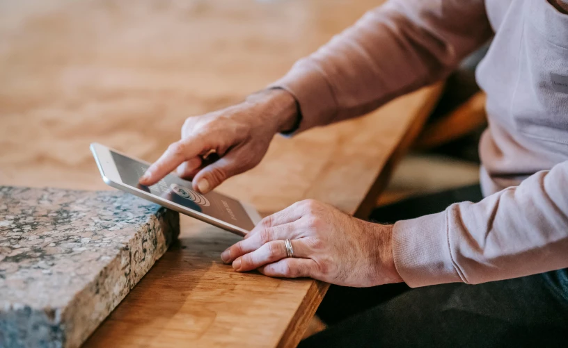 a close up of a person using a cell phone, by Carey Morris, pexels contest winner, arbeitsrat für kunst, stone table, holding a clipboard, bending down slightly, a wooden