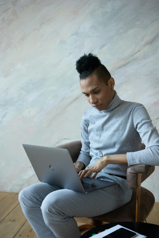 a woman sitting in a chair using a laptop, a portrait, by Carey Morris, trending on unsplash, androgynous male, ashteroth, gray shirt, ignant