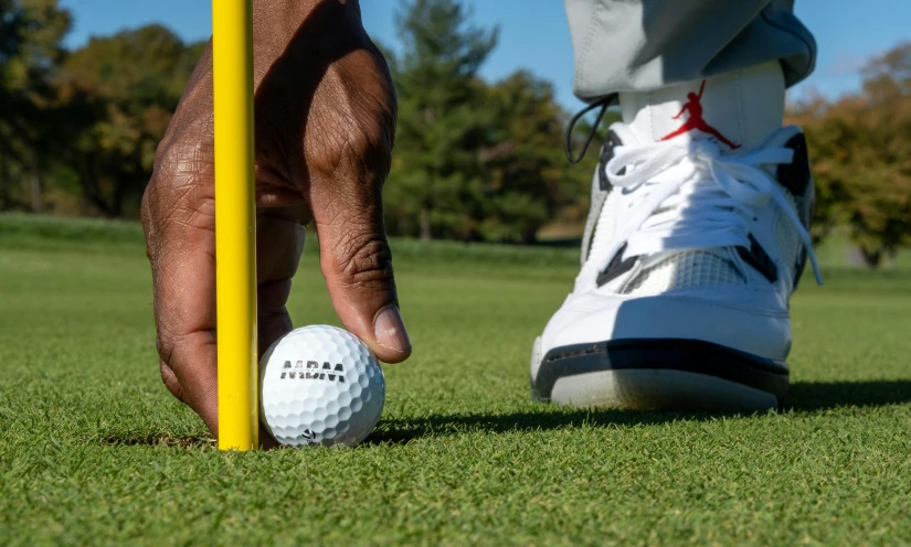 a person holding a golf ball near a yellow pole, “air jordan 1, performance, zoomed in shots, educational