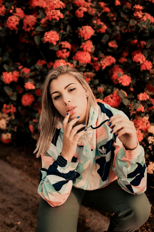 a woman smokes a cigarette in front of a bush of flowers, inspired by Elsa Bleda, unsplash, chappie in an adidas track suit, blonde women, patterned clothing, profile image