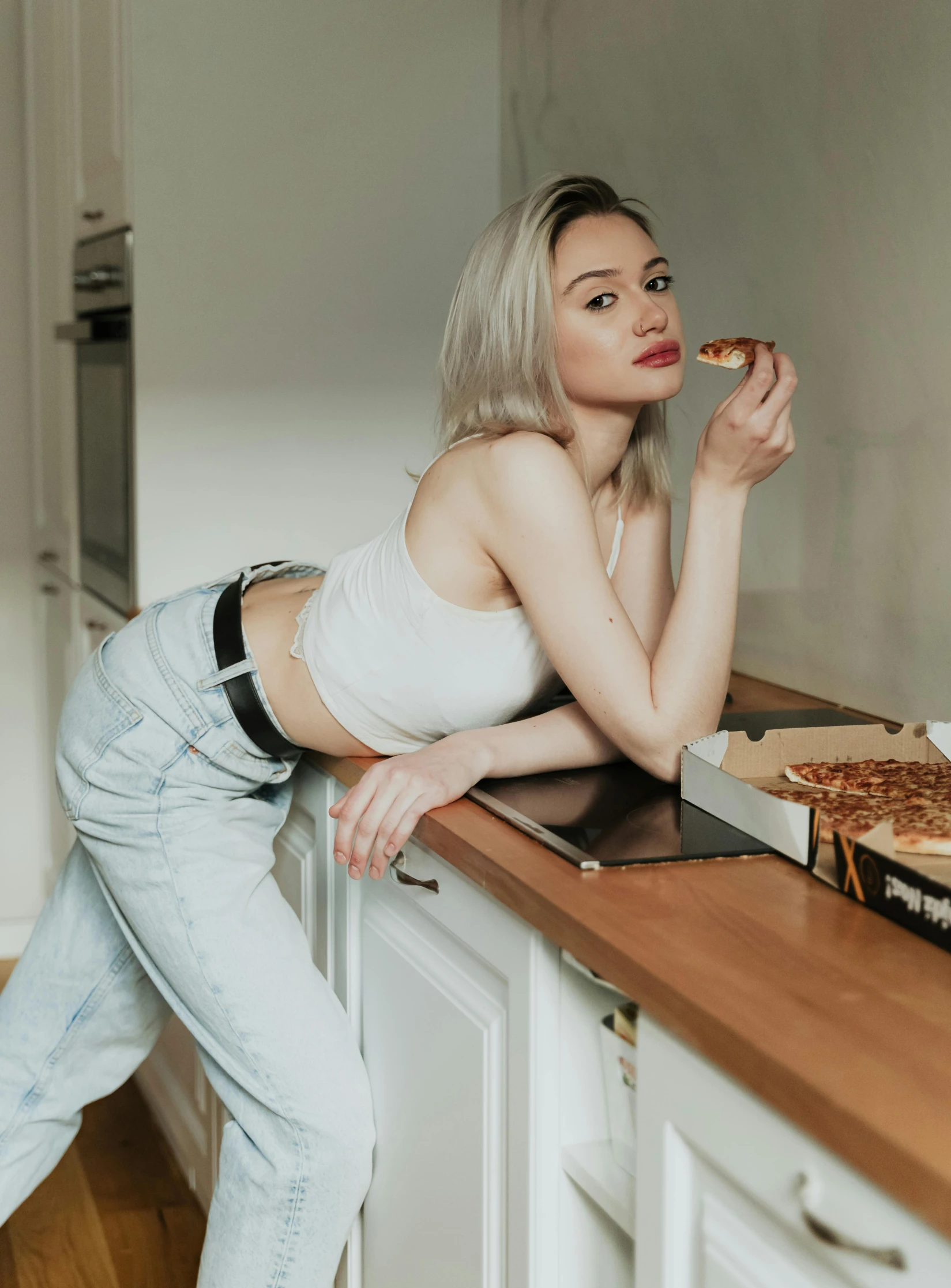 a woman leaning on a counter eating pizza, inspired by Elsa Bleda, trending on pexels, realism, tight outfit, girl silver ponytail hair, better known as amouranth, jeans