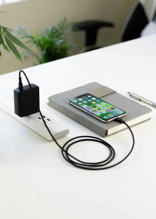 a cell phone sitting on top of a charger next to a plant, square, premium, office, graphite